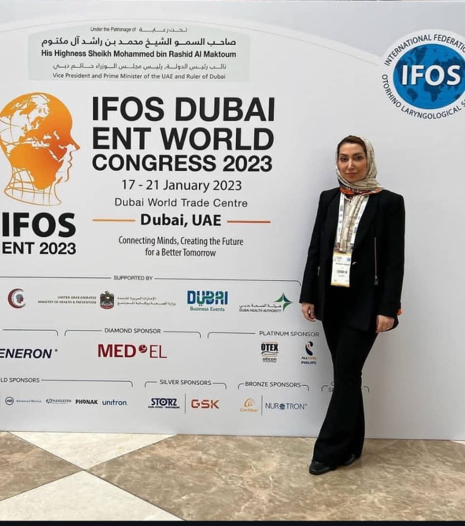 تصویر یک متخصص حوزه گوش، حلق و بینی در مقابل بنر رسمی کنگره جهانی IFOS 2023 در مرکز تجارت جهانی دبی، امارات متحده عربی، در حال ثبت حضور در این رویداد علمی بین‌المللی